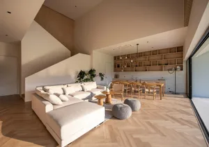 A modern minimalist living room featuring a large beige sectional sofa, wooden floor, and built-in shelving unit.