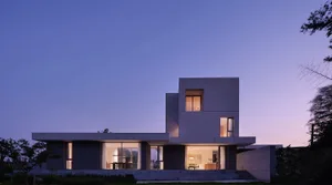 Modern residential house with concrete exterior at dusk with lights on inside