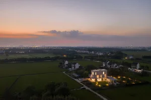 Aerial view of a rural living space with modern architecture and a sunset sky in the background.