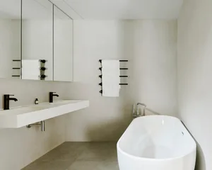 A minimalist bathroom with a concrete accent wall and white porcelain fixtures.