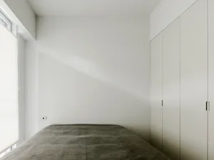A minimalist bedroom features a soft fabric-covered bed against a white wall.