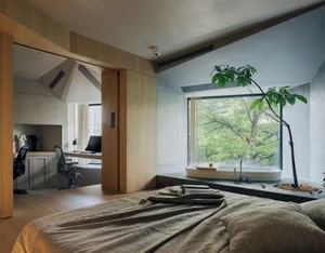 A minimalist bedroom with wood floors, a wooden bed frame, and a large window overlooking greenery.