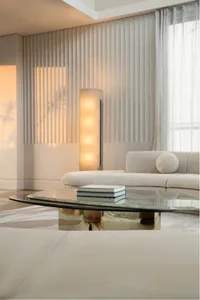 A minimalist living room featuring a white sofa, a glass coffee table, and a fabric curtain with vertical slats