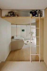 A minimalist loft interior with a wooden staircase leading to a sleeping loft adorned with plush animals.
