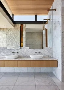 A modern minimalist bathroom featuring a white marble countertop with two sinks, wooden cabinetry, a large mirror, and a larg
