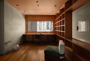 A minimalist study room with wooden furniture, a glass window, and a green cushioned seat.