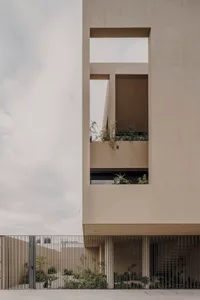 Modern architecture building with sandstone and concrete exterior, featuring large openings and greenery.