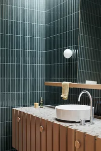 A modern bathroom with concrete tiles, featuring a white circular sink and wooden cabinets.