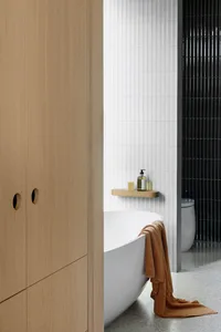 Modern bathroom featuring sleek white tiles, a freestanding bathtub, and wooden cabinets.