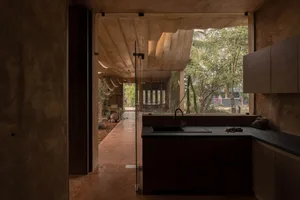 A modern kitchen with concrete walls and a large window overlooking the outdoors.