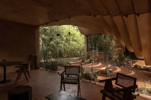 A modern living room with exposed concrete walls and ceiling, featuring large windows with a view of a lush green garden.