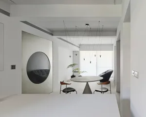 Minimalist dining room with concrete table and chairs, modern hanging lights, and circular mirror on metal panel wall.