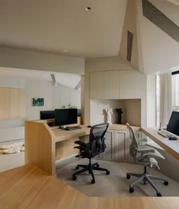 A modern home office featuring a desk with two computer monitors, ergonomic chairs, and storage cabinets.