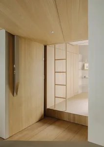 A modern minimalist bedroom with light wood walls and floor, featuring a ladder-like structure leading to a raised sleeping a