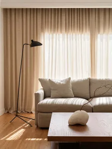 A modern, minimalist living room featuring a sleek fabric couch, wooden coffee table, and floor lamp with a black tripod base