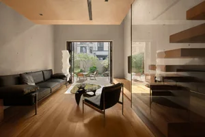 Modern minimalist living room with black and brown furniture, wooden floors, and a glass coffee table.