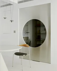 Modern, minimalist living room featuring a metal circular mirror and white floor.