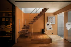 Modern residential interior with wooden stairs, glass railings, and metal accents.