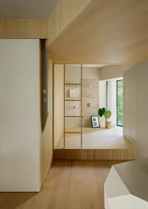 Modern residential space featuring a minimalist library area with wooden shelves and a stairs leading up to a higher level.