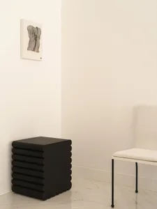 A modern side table with black, cylindrical wood layers against a white wall.