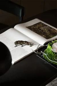 A metal sculpture of a cat on an open book with greenery and a flower arrangement.