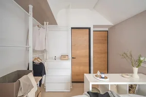 A minimalist bedroom featuring white walls, a white bed frame, and neutral-toned fabrics. Wooden doors and metal shelving are