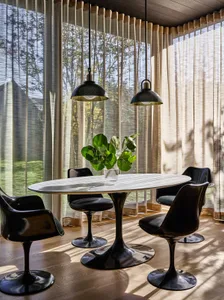 A dining room with black furniture, a round table, and green foliage in a vase.