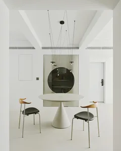 A modern dining room featuring a round table with a cone-shaped base and two chairs with black seats and wooden backs.
