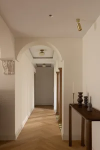 A modern hallway with wooden flooring, arched doorways, and a console table with decorative objects.