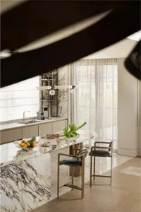 Modern kitchen featuring marble countertops and white chairs with a hanging light fixture and cityscape view.