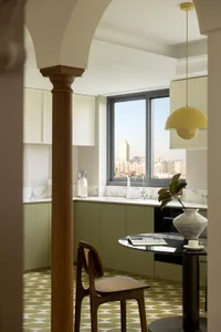 A modern kitchen with marble countertops and floor tiles, featuring a sink, cabinets, and a table with a vase and coffee setu