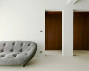 A modern living room with a gray concrete sofa, white walls, and wooden doors.