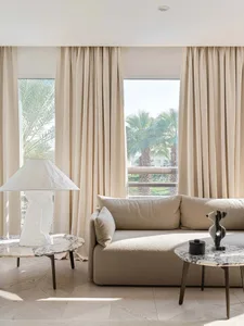 Modern living room featuring a fabric sofa and marble tables with a view of palm trees outside.