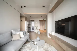 Modern living room featuring white walls, a grey sofa with white and beige throw pillows, and a wooden floor. A white coffee