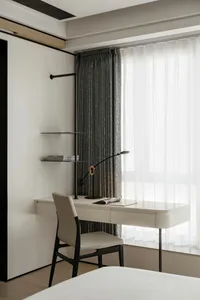 A minimalist bedroom workspace with a white desk and chair, a modern lamp, and a window with gray curtains.