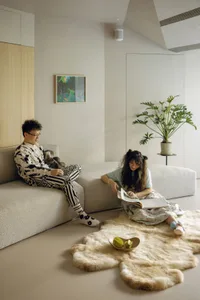 A modern minimalist living room with concrete walls, leather furniture, and plush textiles.
