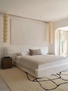 Minimalist bedroom with a large white bed, neutral fabrics, and a geometric patterned rug.
