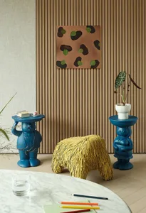 A vibrant room featuring two blue anthropomorphic side tables and a yellow textured stool.