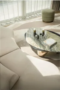 A modern living room featuring a marble coffee table with candles and a book, upholstered furniture, and a patterned rug.