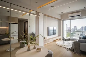 A modern minimalist living room with a round table, grey sofa, and large windows providing a view of the city.
