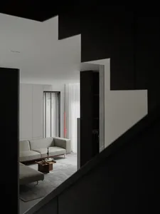 Contemporary modern minimalist living room with white furniture and dark staircase.