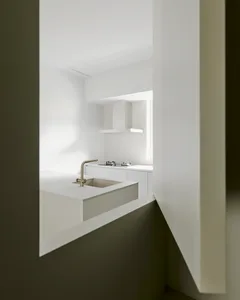 A modern kitchen with white countertops and walls, featuring a stainless steel faucet and a gas stove.