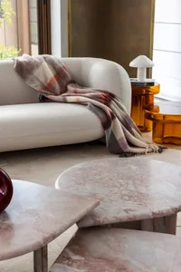 A modern living room with a sleek marble coffee table, plush textiles draped over the furniture, and ambient lighting.