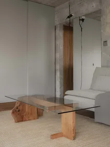 Modern industrial interior living room with glass table, wooden elements, and concrete walls.