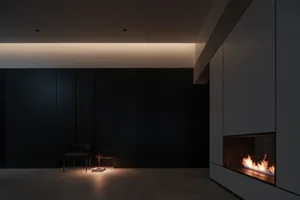 A minimalist living room featuring a concrete floor and walls, with a cozy fireplace and a solitary chair.