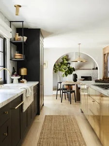 A modern kitchen featuring black and gold cabinets, marble countertops, and brass accents.
