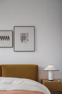 Modern minimalist bedroom featuring a yellow upholstered headboard against a white wall, with framed art hanging above a bed 