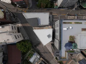 Urban architecture with a rooftop garden featuring a white triangular structure and a green space with umbrellas.