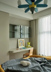 A minimalist bedroom with white furniture, a blue and gray striped blanket, and a yellow teddy bear on the desk.