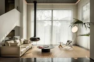 A modern minimalist living room with large glass windows, a sleek sofa, and a central coffee table.